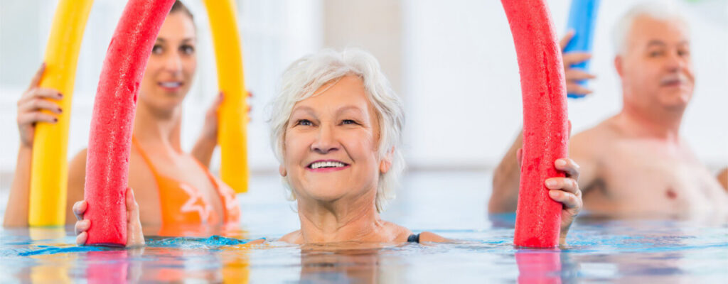 Geriatric female in swimming pool using a pool noodle as part of aquatic therapy treatment.