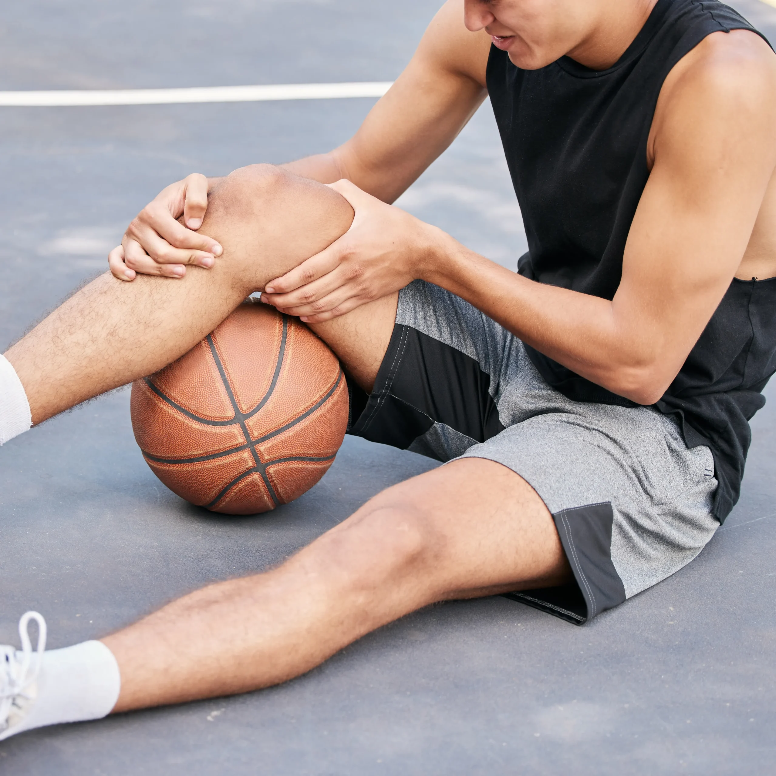 man holds his knee after injuring it during a basketball game
